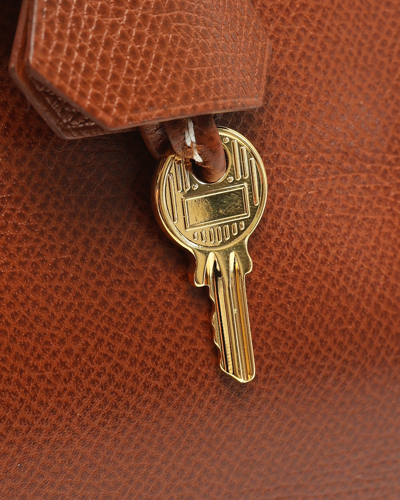 A detailed close-up of the gold-toned key from the Hermès Birkin 30 bag, resting against the brown Courchevel leather.