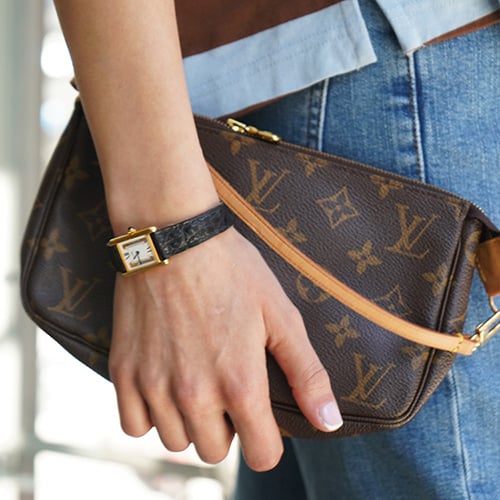 A Louis Vuitton Speedy 30 handbag in Damier Azur canvas with natural leather handles, adorned with a beige fur pom-pom and leather tassel charm, resting on a beige leather car seat.