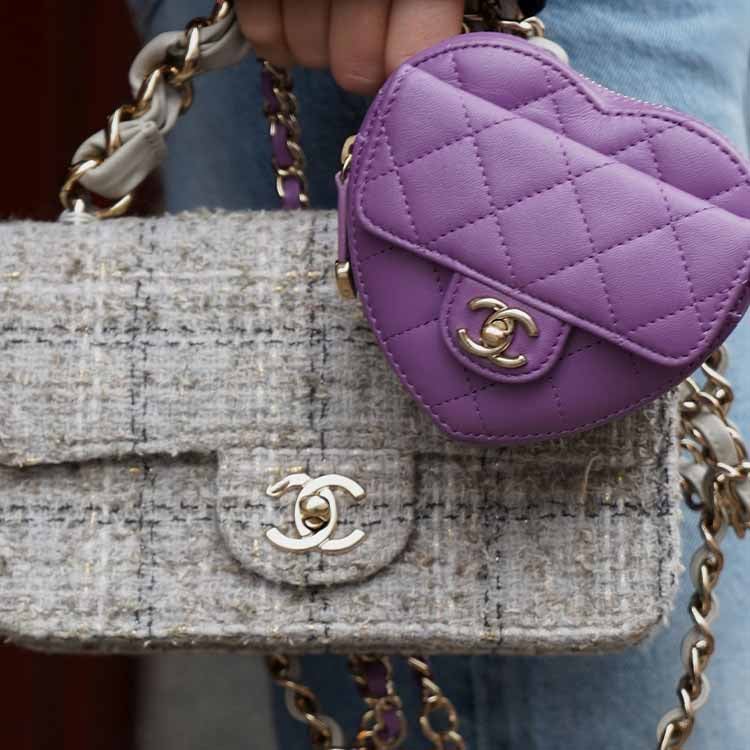 A hand holding a yellow Chanel quilted clutch bag in sunlight, featuring the signature CC turn-lock closure and a gold chain strap, with shadows cast on a light wall in the background.