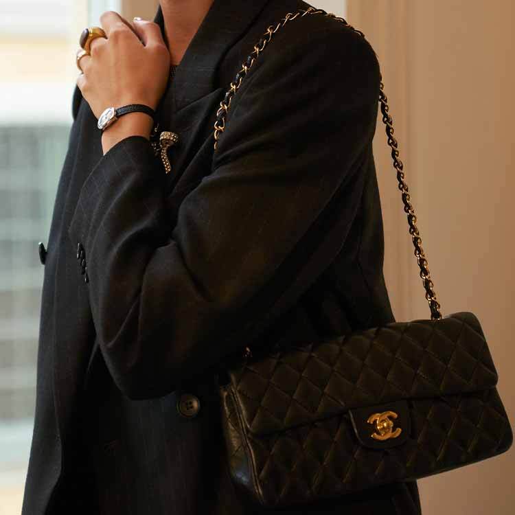 A hand holding a yellow Chanel quilted clutch bag in sunlight, featuring the signature CC turn-lock closure and a gold chain strap, with shadows cast on a light wall in the background.