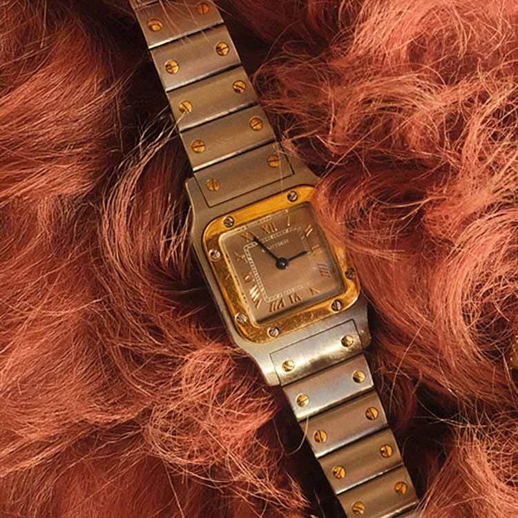 A gold and silver wristwatch and several delicate gold necklaces displayed on a soft, textured pink fabric background.