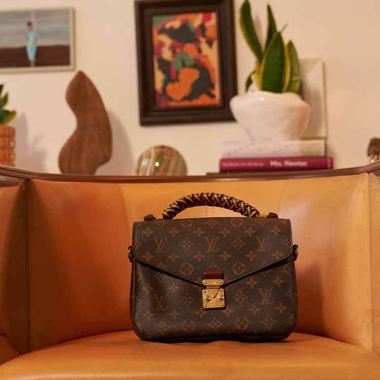 A Louis Vuitton Speedy 30 handbag in Damier Azur canvas with natural leather handles, adorned with a beige fur pom-pom and leather tassel charm, resting on a beige leather car seat.