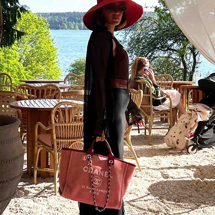 Person in red hat and dark outfit holding a pink Chanel shopping bag outdoors at a café.