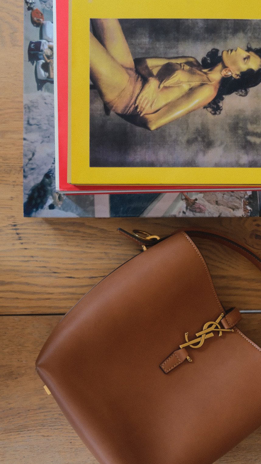 A person wearing a brown knit sweater carries a black Loewe leather shoulder bag with a silver chain detail.