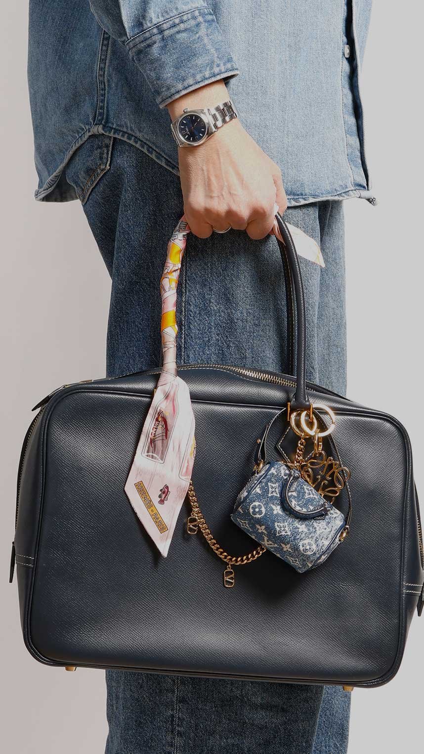 Person i jeans håller blå väska med scarf och blå Louis Vuitton-miniväska.