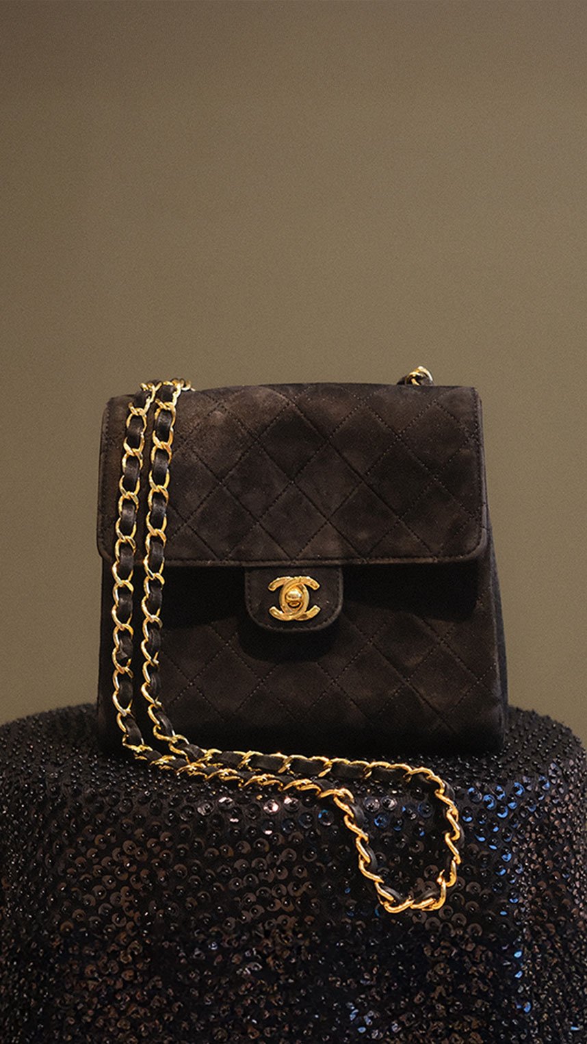 Elegant black shoulder bag with a gold-tone clasp, placed on a decorative table with a black and wood sunburst pattern.