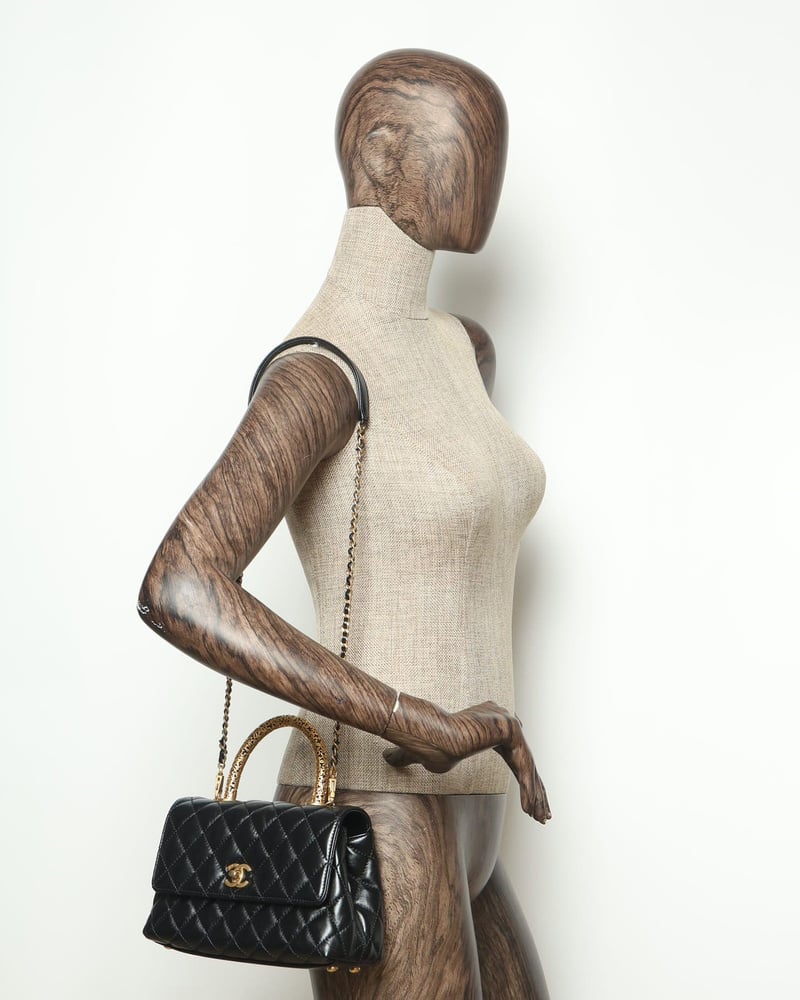 Angled view of a black Chanel Small Signature Coco Handle Bag, worn on a mannequin's shoulder to demonstrate scale.
