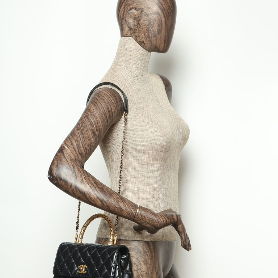 Angled view of a black Chanel Small Signature Coco Handle Bag, worn on a mannequin's shoulder to demonstrate scale.