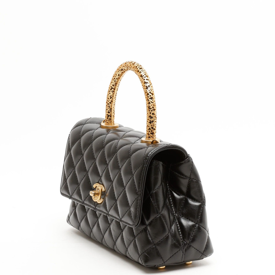Front view of a Chanel Small Signature Coco Handle Bag in black quilted leather, highlighting its ornate gold-tone handle.
