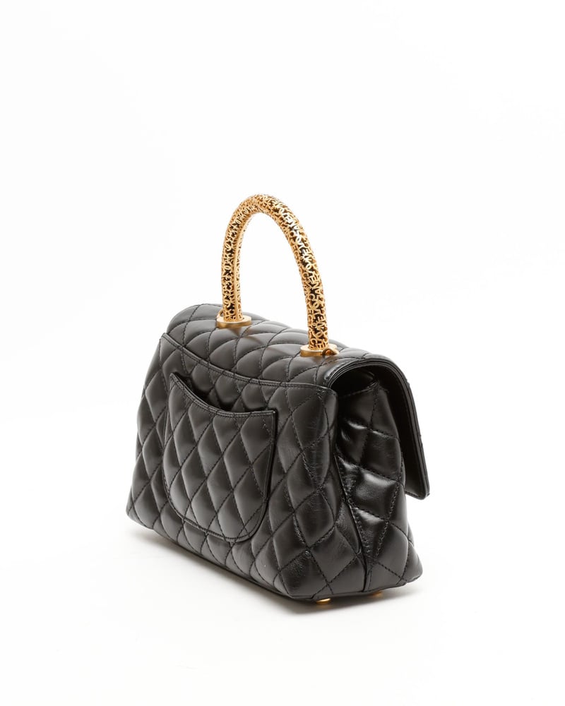 Angled back view of a Chanel Small Coco Handle Bag in black quilted leather, showcasing its ornate gold-tone handle.