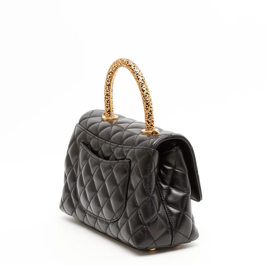 Angled profile of a Chanel Small Signature Coco Handle Bag in black quilted leather, showing its ornate gold-tone handle.