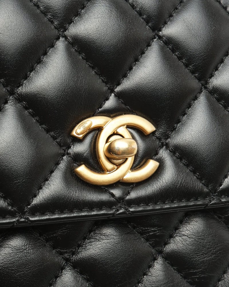 Close-up of the gold-tone CC turn-lock clasp on the black diamond-quilted leather of a Chanel Small Coco Handle Bag.
