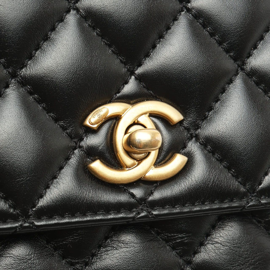 Close-up of the gold-tone CC turn-lock clasp on the black diamond-quilted leather of a Chanel Small Coco Handle Bag.