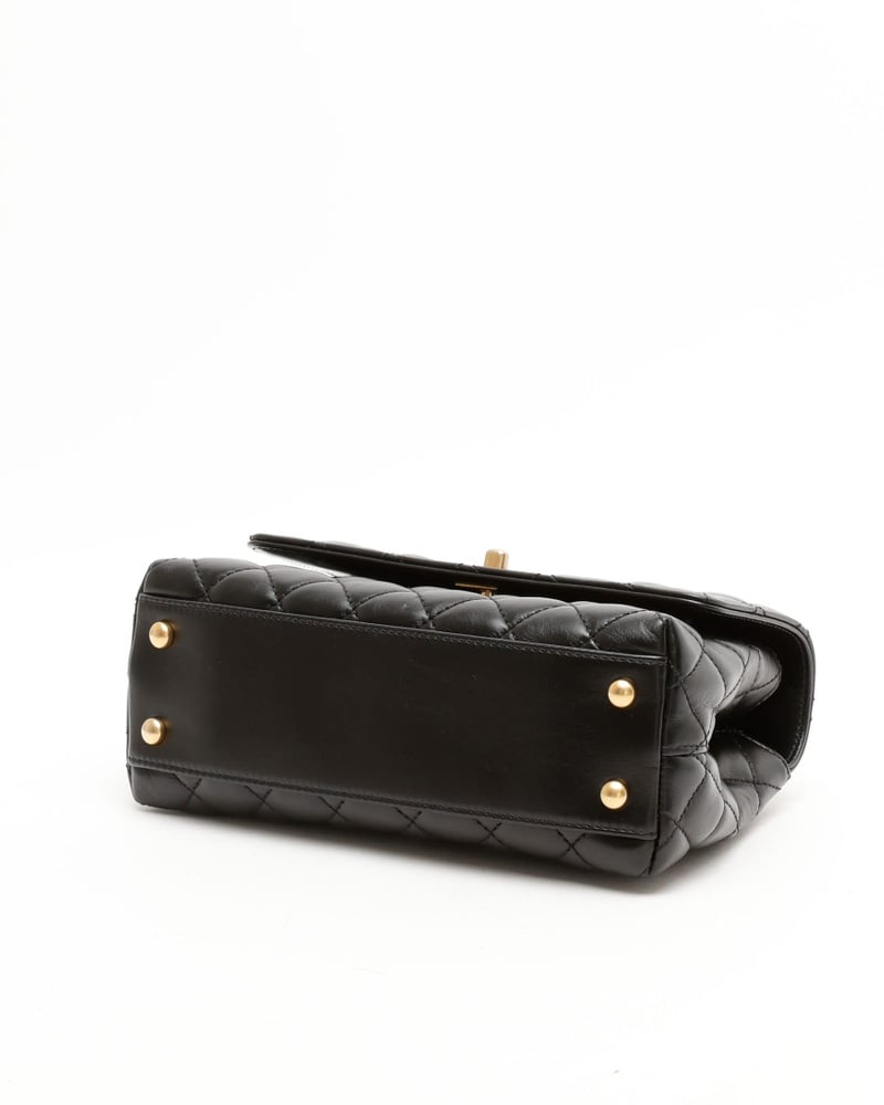 Bottom view of a black Chanel Small Coco Handle Bag in quilted leather, highlighting its four gold-tone protective feet.