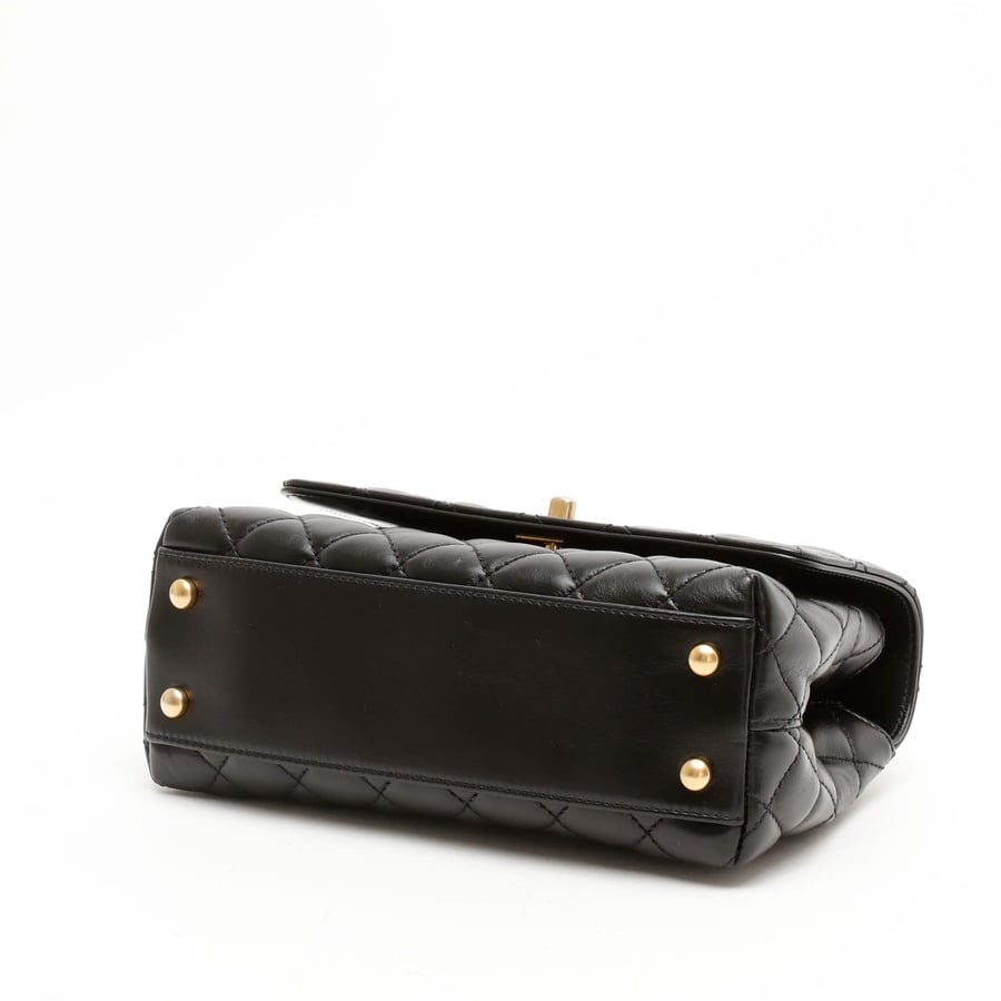 Bottom view of a black Chanel Small Coco Handle Bag in quilted leather, highlighting its four gold-tone protective feet.