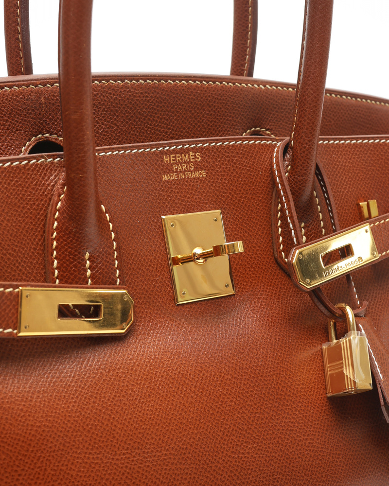Angled close-up of the Hermès Birkin 30's gold-toned closure, lock, and brand stamp on brown Courchevel leather.