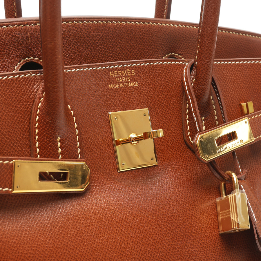 Angled close-up of the Hermès Birkin 30's gold-toned closure, lock, and brand stamp on brown Courchevel leather.