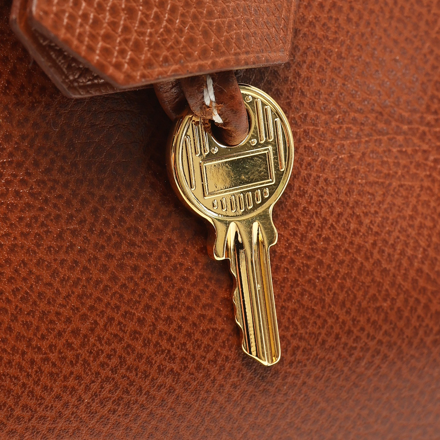 A detailed close-up of the gold-toned key from the Hermès Birkin 30 bag, resting against the brown Courchevel leather.