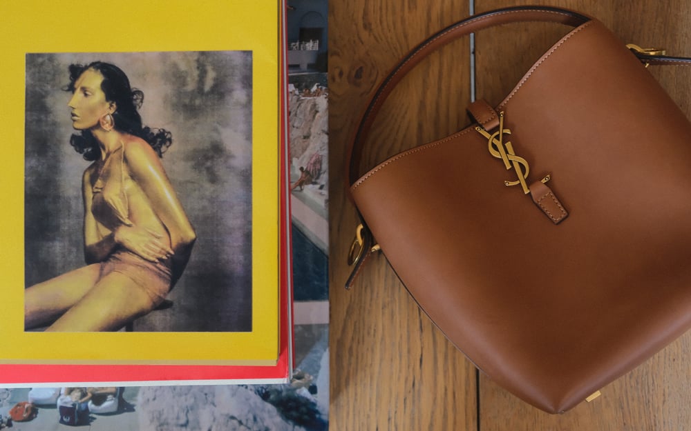 A person wearing a brown knit sweater carries a black Loewe leather shoulder bag with a silver chain detail.