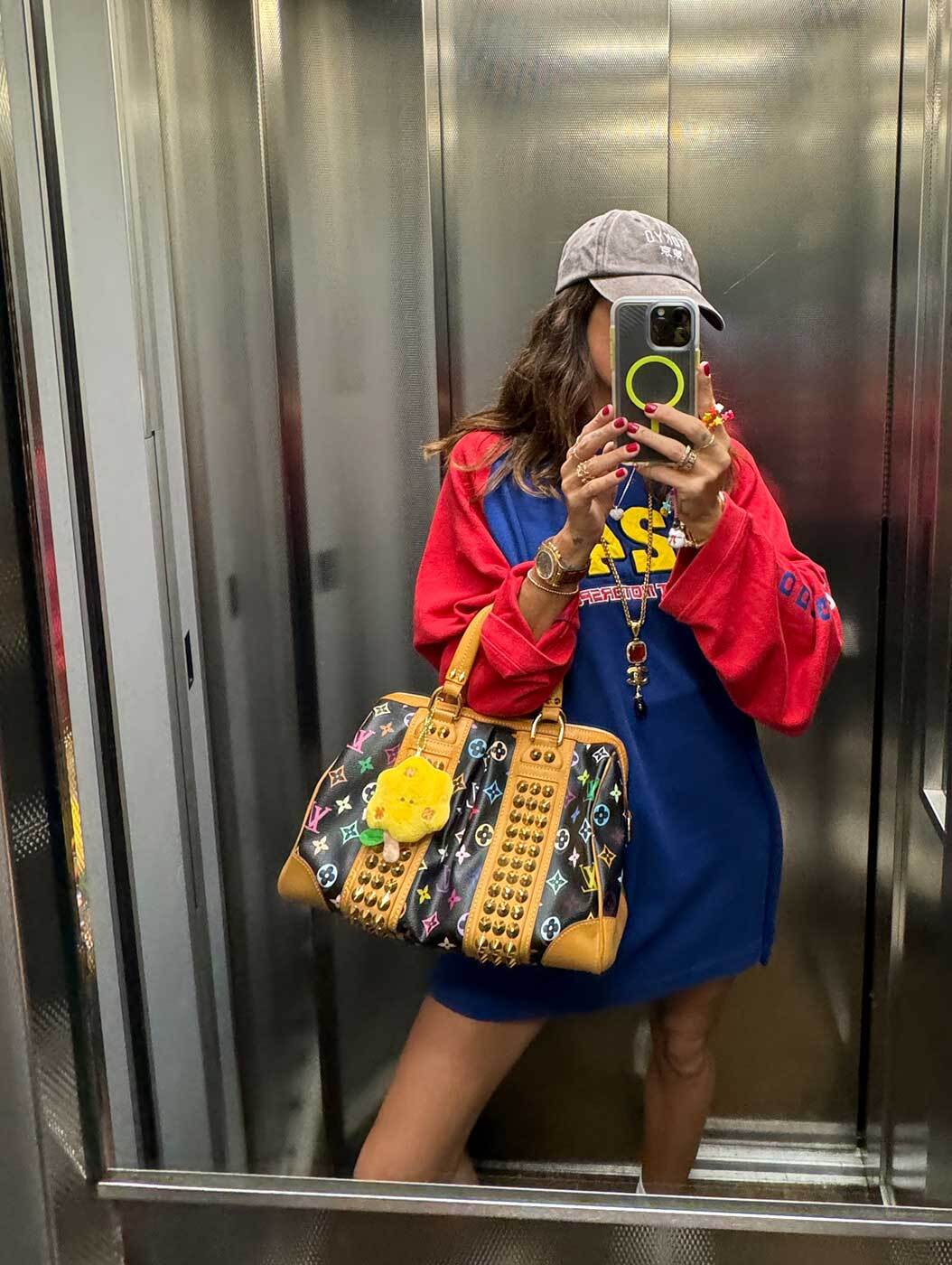 Hand holding Louis Vuitton bag with studs and colorful charms.