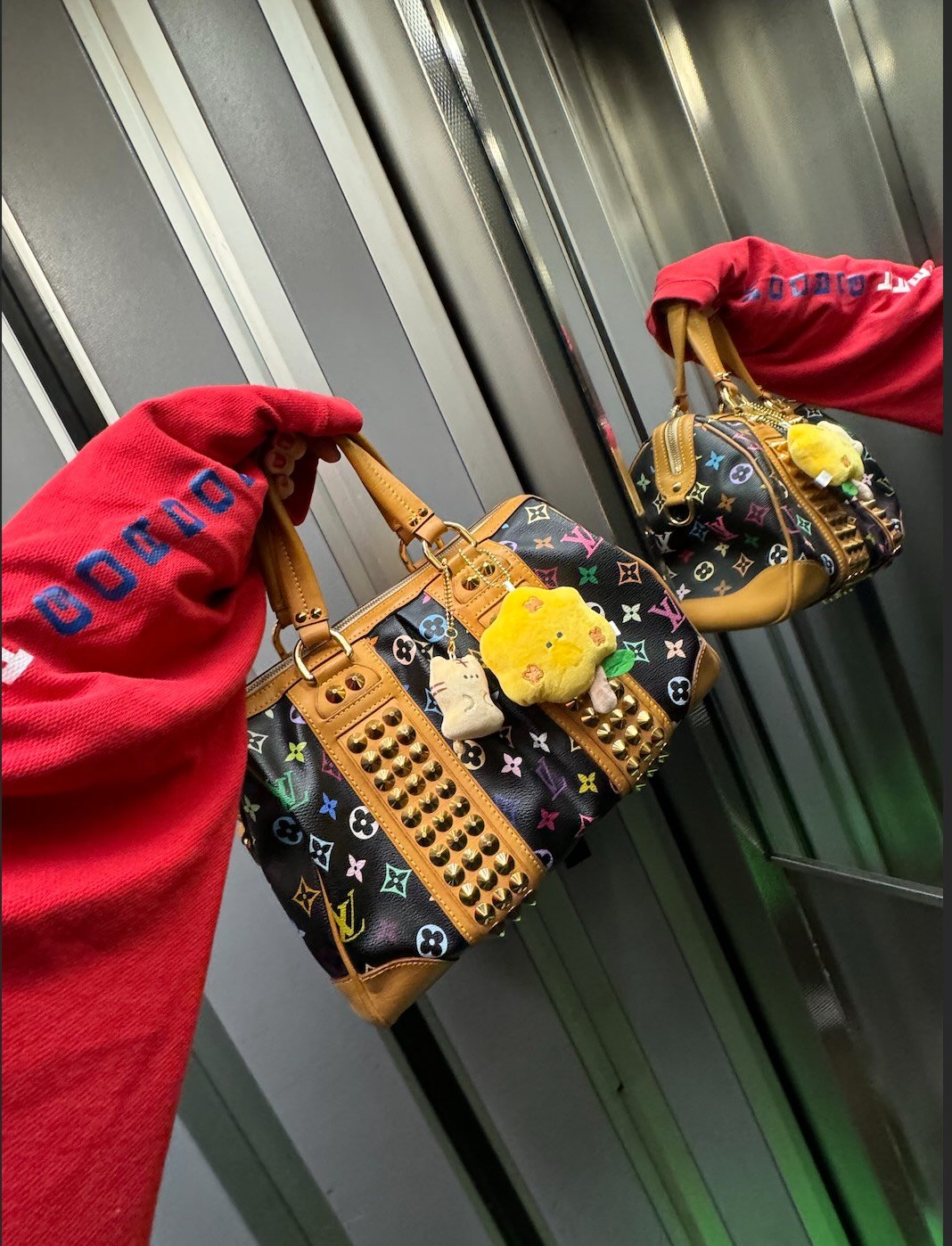 Hand håller Louis Vuitton-väska med nitar och färgglada berlocker.