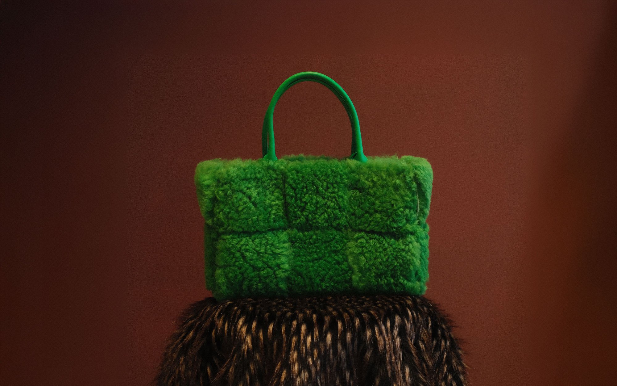 A person wearing a brown knit sweater carries a black Loewe leather shoulder bag with a silver chain detail.