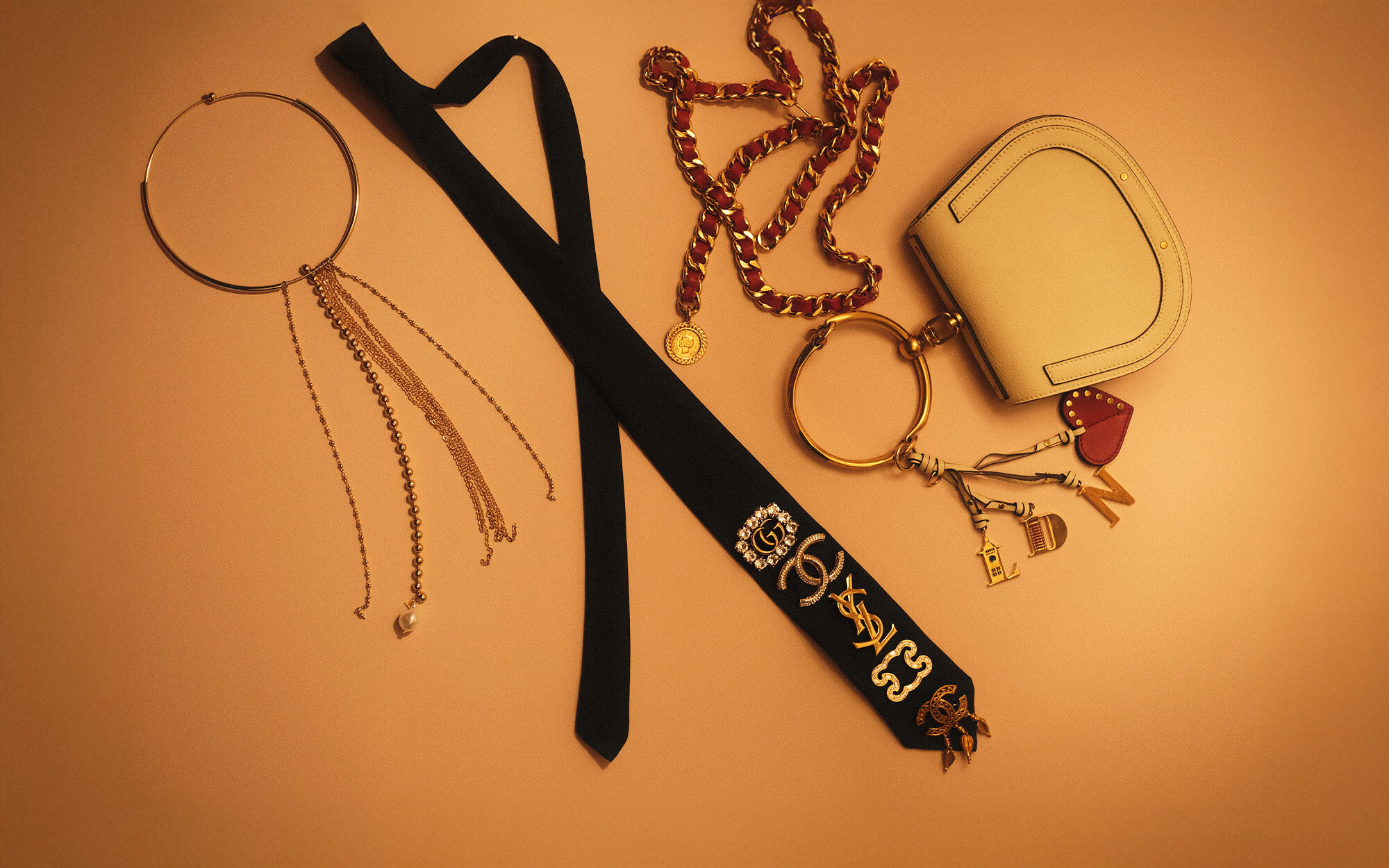 A person dressed in an elegant black outfit and veiled hat, accessorized with statement earrings and brooches. In the first view, they smile while holding a quilted black handbag with gold hardware. In the second view, they stand by a window, reaching toward the handbag resting on a stack of books.