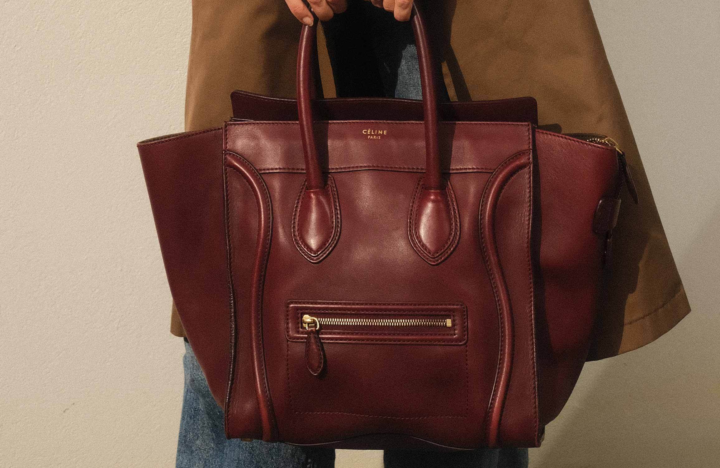 Close-up of a person holding a burgundy Céline leather handbag, styled with a brown trench coat and jeans.