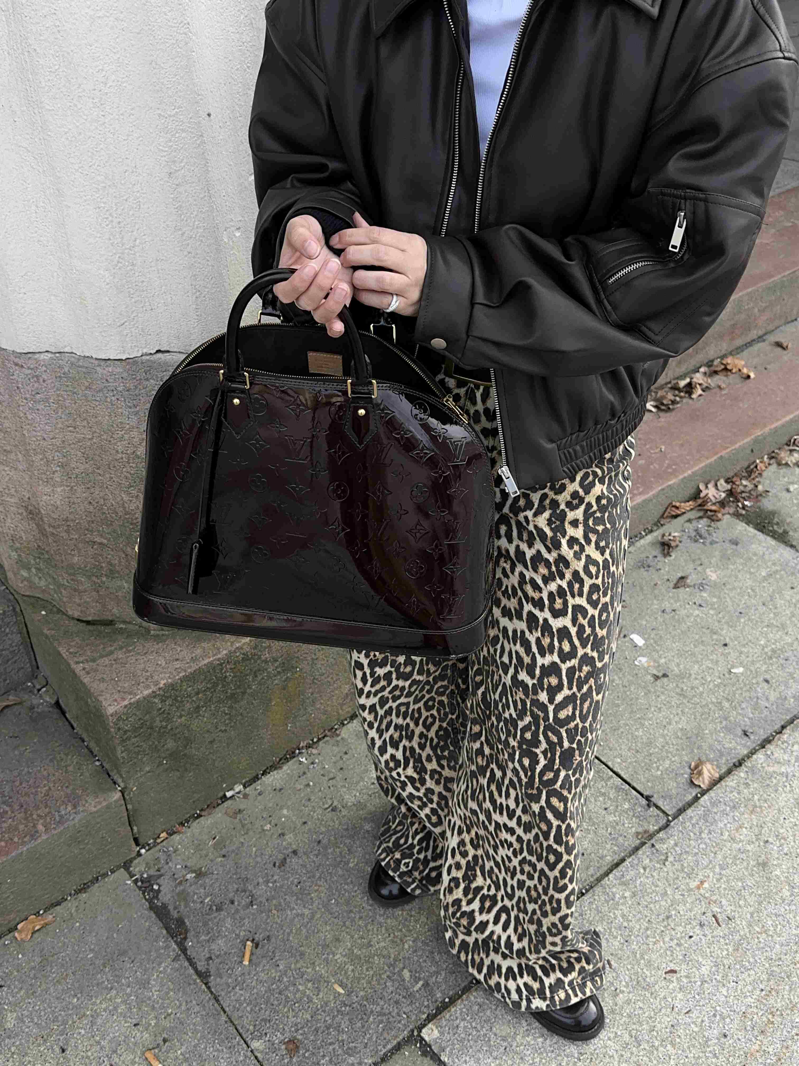 Person i skinnjacka med leopardbyxor håller mörk Louis Vuitton-väska.
