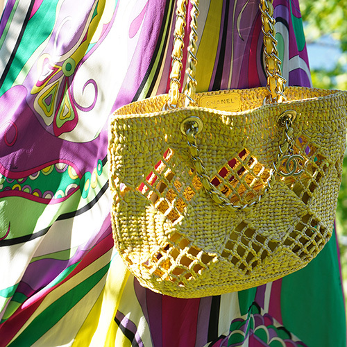 Woman in light jacket and sunglasses holding a brown Louis Vuitton bag with a patterned scarf.