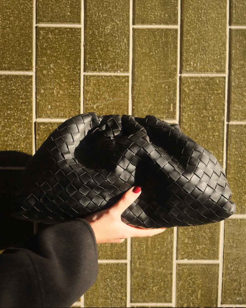 Woman in light jacket and sunglasses holding a brown Louis Vuitton bag with a patterned scarf.