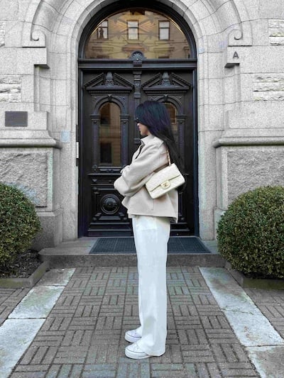 Woman in light jacket and white pants with beige Chanel shoulder bag in front of a doorway.