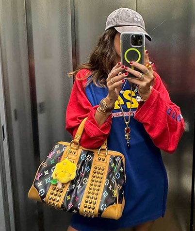 Person in colorful outfit taking selfies in an elevator with a black Louis Vuitton bag featuring studs and patterns.