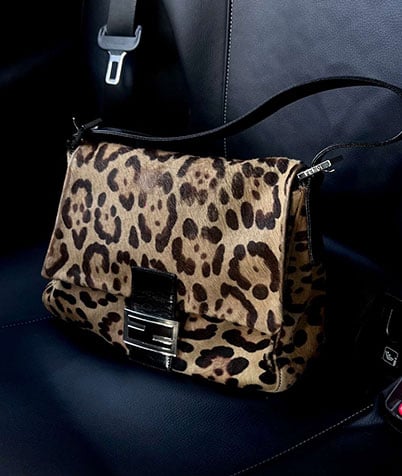 Leopard-print Fendi bag with black shoulder strap lying on a black leather car seat.
