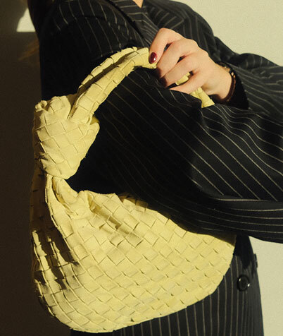 Woman in light jacket and sunglasses holding a brown Louis Vuitton bag with a patterned scarf.