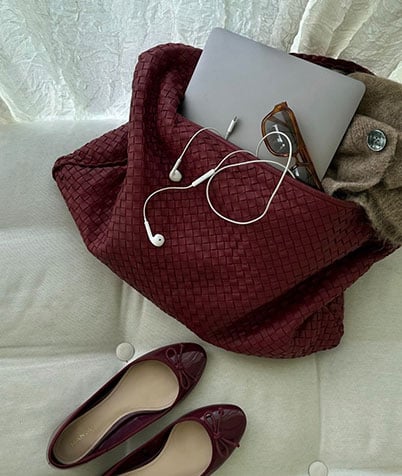 Burgundy Bottega Veneta bag with laptop, glasses and earphones on a light sofa.