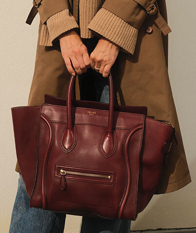 Burgundy Bottega Veneta bag with laptop, glasses and earphones on a light sofa.