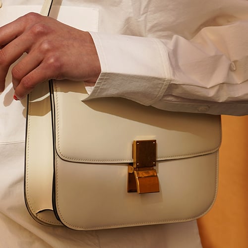 Woman in light jacket and sunglasses holding a brown Louis Vuitton bag with a patterned scarf.