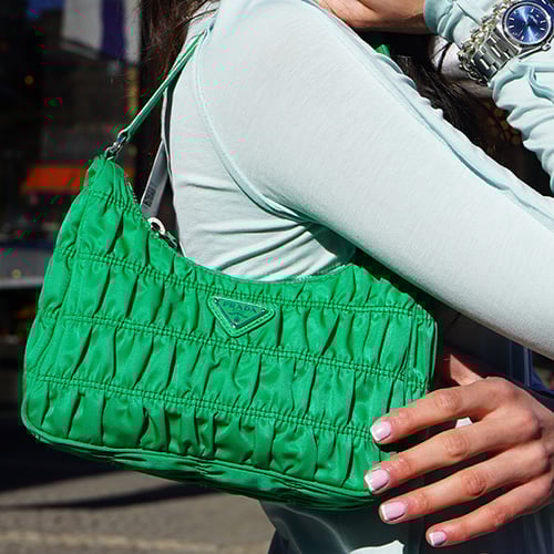 Woman in light jacket and sunglasses holding a brown Louis Vuitton bag with a patterned scarf.