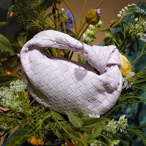 Burgundy Bottega Veneta bag with laptop, glasses and earphones on a light sofa.