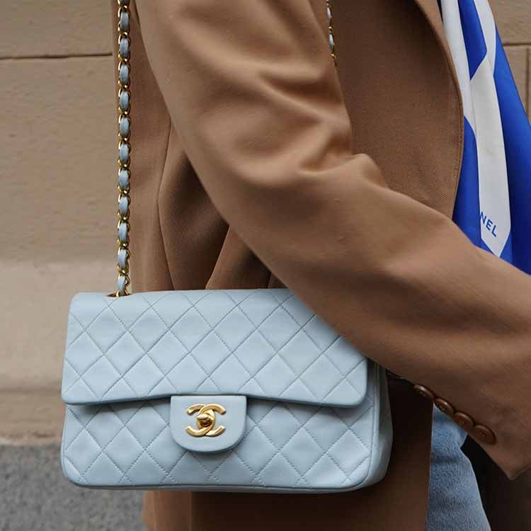 Burgundy Bottega Veneta bag with laptop, glasses and earphones on a light sofa.