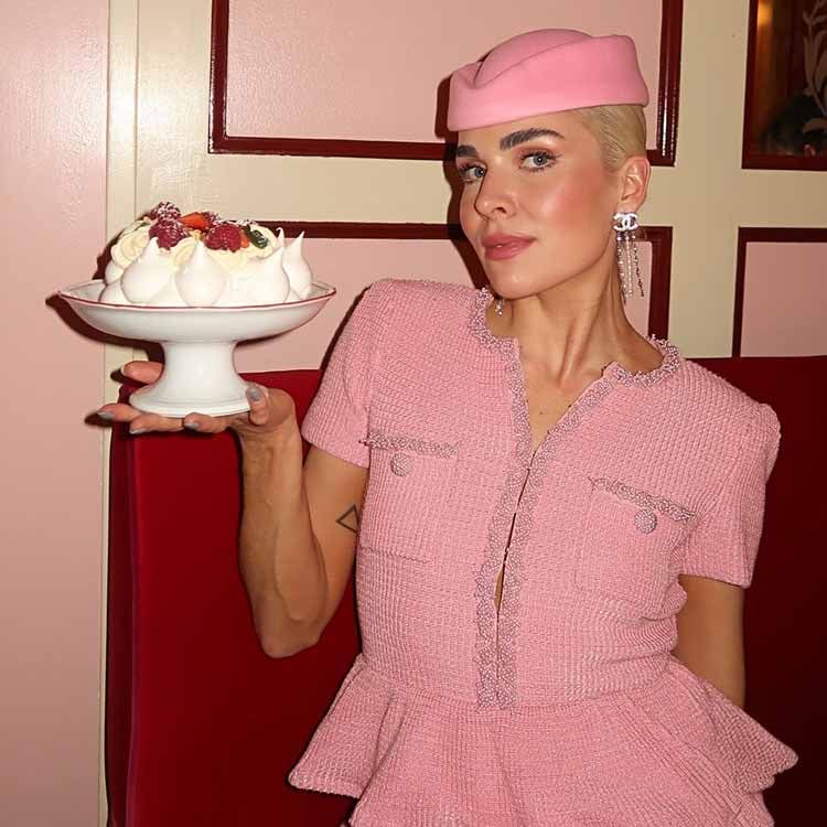 Woman in light jacket and sunglasses holding a brown Louis Vuitton bag with a patterned scarf.