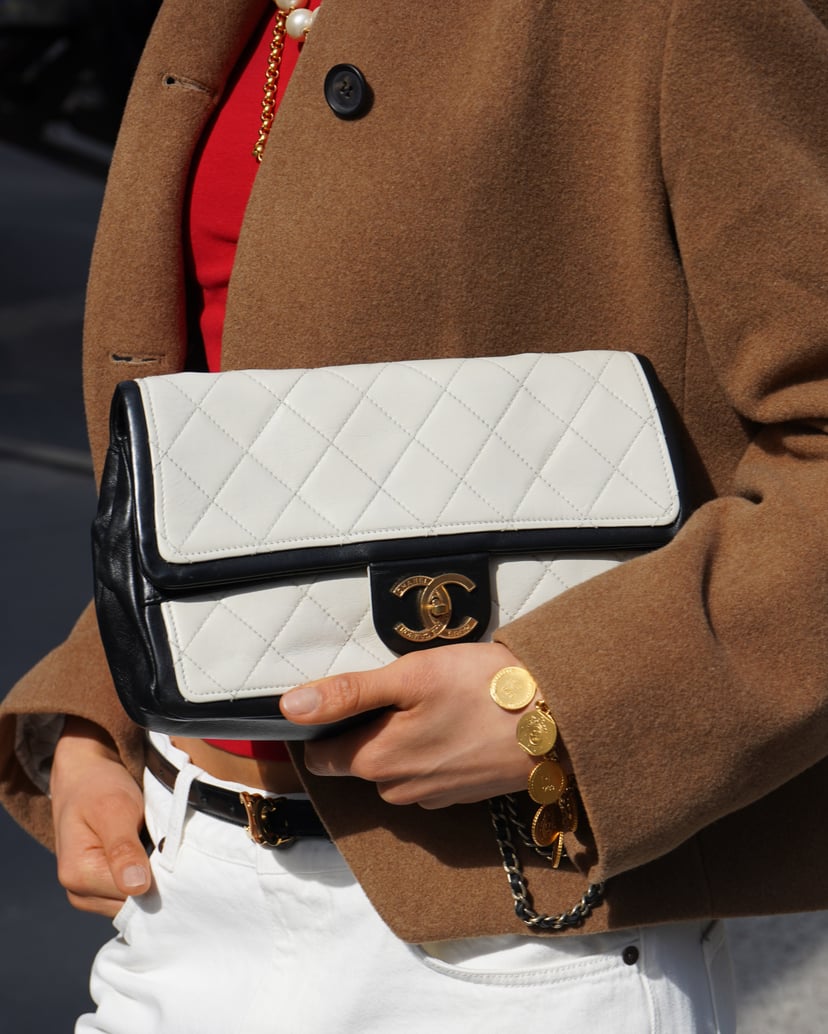 Woman in light jacket and white pants with beige Chanel shoulder bag in front of a doorway.